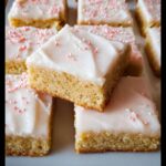 Close-up of several squares of delicious gluten-free sugar cookie bars topped with white frosting and pink sprinkles.