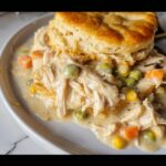 Close-up of creamy Comfort Food Chicken Pot Pie Slow Cooker filling with shredded chicken, peas, carrots, and a biscuit on top.