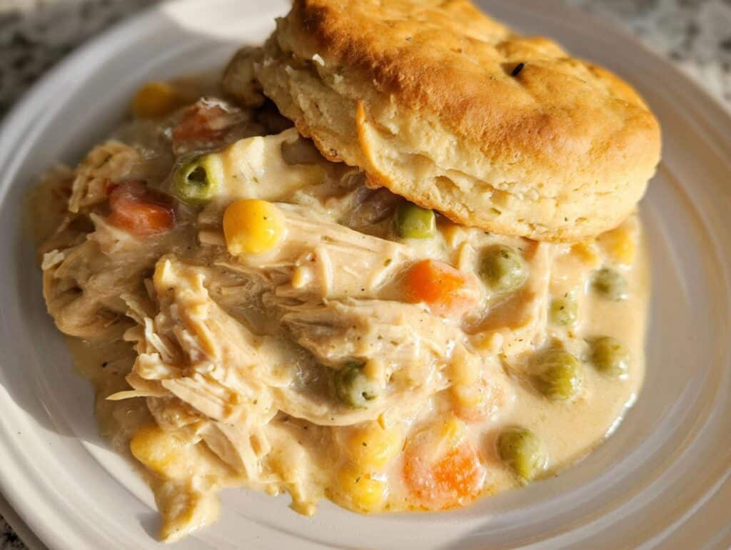 A serving of creamy Comfort Food Chicken Pot Pie Slow Cooker filling topped with a golden biscuit.
