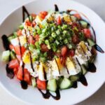 A vibrant Cottage Cheese & Cucumber Snack Plate featuring cottage cheese, sliced hard-boiled eggs, diced tomatoes, cucumbers, and green onions.