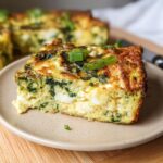 A square slice of baked Cottage Cheese Egg Bake with visible spinach and cottage cheese curds, topped with green onions.