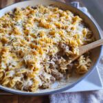 A close-up of a skillet filled with baked Creamy Beef Noodle Casserole, topped with melted and shredded cheese.