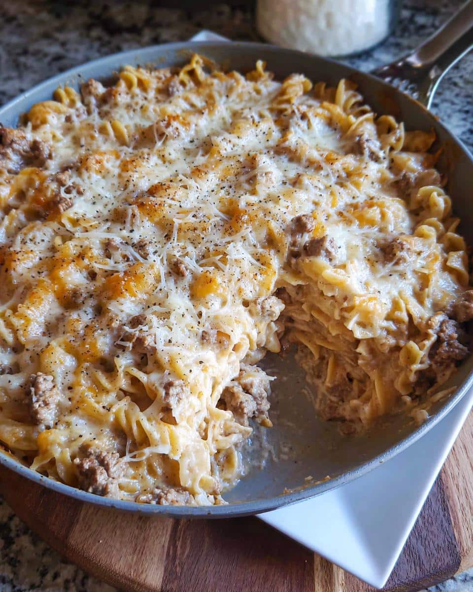 A close-up of a skillet filled with baked Creamy Beef Noodle Casserole topped with melted cheese and pepper.