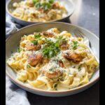 Close-up of a bowl of creamy garlic chicken pasta featuring fettuccine, pan-seared chicken pieces, and fresh parsley.