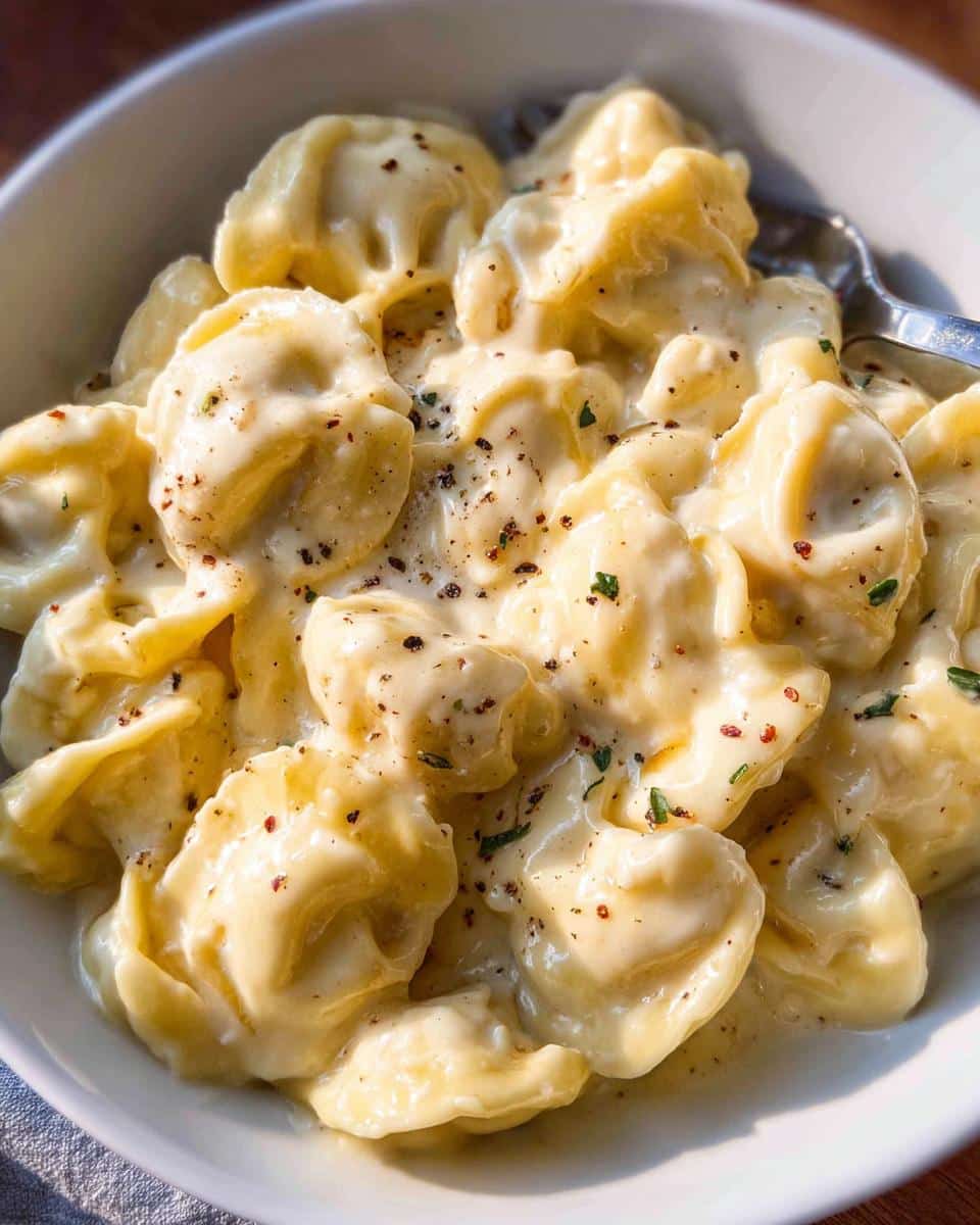 Close-up of tortellini pasta generously coated in a rich, creamy garlic sauce, seasoned with pepper flakes and herbs.