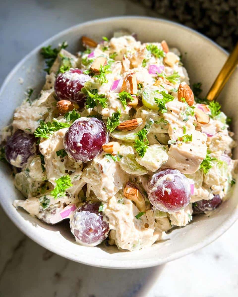 Close-up of creamy Greek Yogurt Chicken Salad mixed with red grapes, sliced almonds, and fresh parsley.