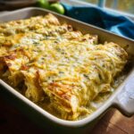 Close-up of baked Creamy Green Chile Chicken Enchiladas covered in melted cheese and parsley in a baking dish.