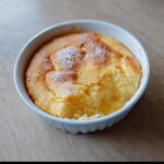 A single serving of golden-topped Creamy Lemon Thermomix Pudding in a white ramekin, showing a soft interior.
