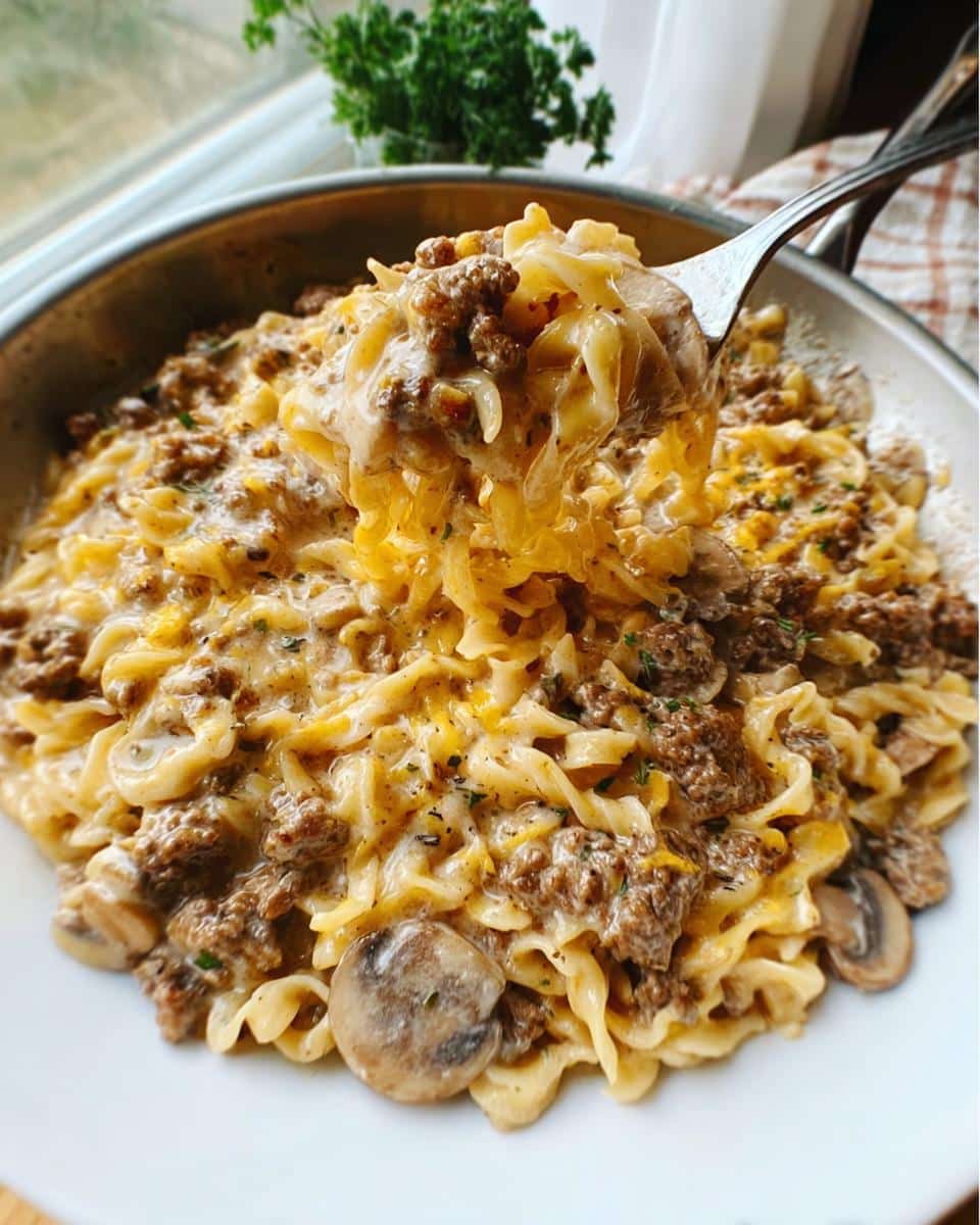 A fork lifting a generous portion of Creamy Mushroom Ground Beef Casserole, showing pasta, ground beef, and creamy sauce.