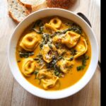 A close-up of a bowl of Creamy Pumpkin Tortellini Fall Soup topped with pumpkin seeds and parmesan.