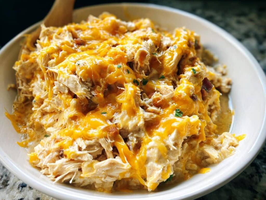 Close-up of shredded chicken mixed with creamy sauce and topped with melted cheddar cheese, representing Creamy Ranch Crack Chicken.