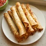 A pile of golden, baked Dairy-Free Chicken Taquitos arranged on a white plate.