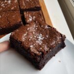 A close-up of a fudgy Dark Chocolate Espresso Brownie square topped with flaky sea salt.