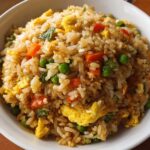 A close-up, top-down view of a bowl filled with Easy Fried Rice with Eggs & Vegetables, showing rice, scrambled egg pieces, peas, and diced carrots.