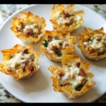 Six golden Easy Sausage Phyllo Cups filled with savory sausage and topped with melted cheese, arranged on a white serving plate.