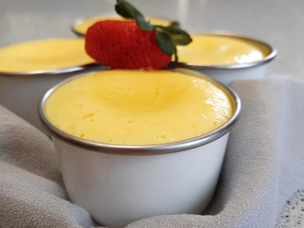 Close-up of creamy yellow Easy TM6 Vanilla Custard Pots topped with a fresh strawberry.