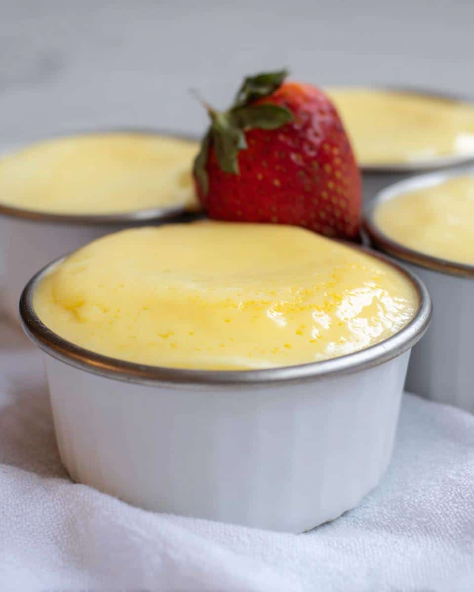 Close-up of Easy TM6 Vanilla Custard Pots in white ramekins, topped with a fresh strawberry.