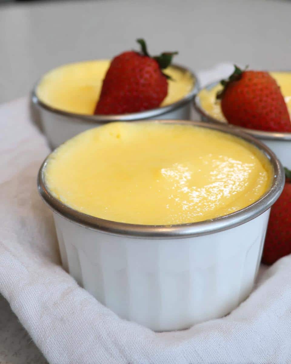 Three white ramekins filled with smooth, yellow Easy TM6 Vanilla Custard Pots, each topped with a fresh strawberry.