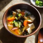 A steaming bowl of Easy Vegetable Miso Soup featuring tofu, carrots, seaweed, and green onions.