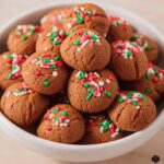 A close-up of many small, round Gingerbread Cookie Bites topped with red, green, and white holiday sprinkles.
