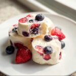 Close-up of stacked Frozen Yogurt Berry Bites studded with strawberries and blueberries on a white plate.