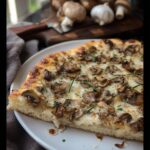A close-up slice of Garlic Mushroom White Pizza showing a thick crust, melted cheese, and sautéed mushrooms topped with fresh chives.