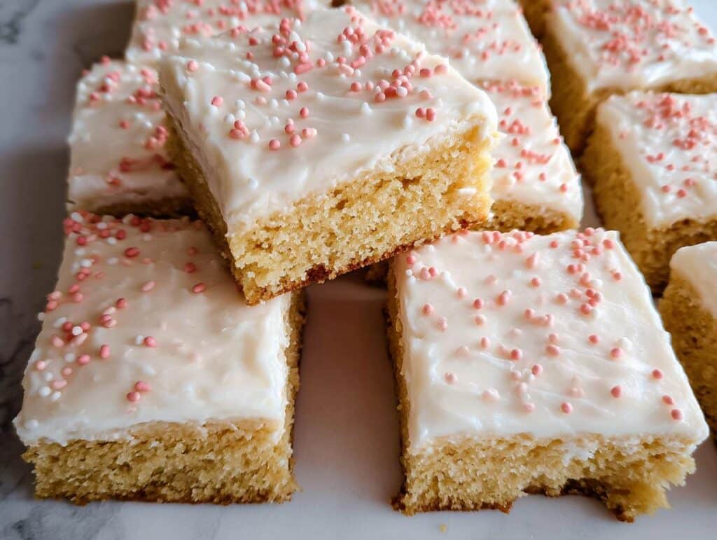 Close-up of several squares of gluten-free sugar cookie bars topped with white frosting and pink sprinkles.