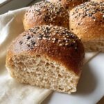Close-up of a Gluten-free and Yeast-free Breakfast Bun cut in half, showing the soft crumb and sesame seed topping.