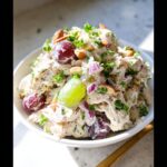 A bowl of creamy Greek Yogurt Chicken Salad mixed with red onion, almonds, and whole red and green grapes.