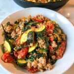 A white bowl filled with Ground Turkey & Veggie Skillet Lunch featuring ground turkey, zucchini slices, and spinach.