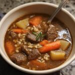 Close-up of a hearty bowl of Beef & Barley Soup with chunks of beef, carrots, potatoes, and barley in rich broth.