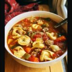Close-up of a white bowl filled with Hearty Sausage Tortellini Minestrone soup, featuring tortellini, sausage, and vegetables in a rich broth.
