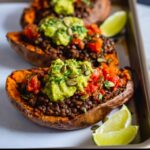 Close-up of a High Protein Lentil Stuffed Sweet Potato topped with chunky guacamole and pumpkin seeds.
