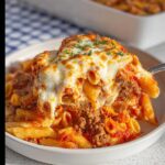 A serving spoon lifting a cheesy portion of Italian Ground Beef Marinara Pasta Bake, showing melted mozzarella and ground meat sauce.