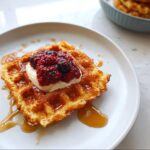 A golden brown Keto Breakfast Chaffle topped with cream, mixed berries, and drizzled with syrup.
