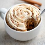 A spoonful being taken from a Keto Cinnamon Breakfast Mug Cake topped with cream cheese frosting and cinnamon.