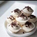 A stack of white Keto Cream Cheese Fat Bombs topped with dark chocolate shavings on a white plate.