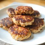 A stack of golden-brown, pan-fried Keto Turkey Breakfast Patties piled on a white plate.