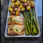 Two fillets of Lemon Garlic Salmon with Asparagus and roasted potatoes on a white platter.
