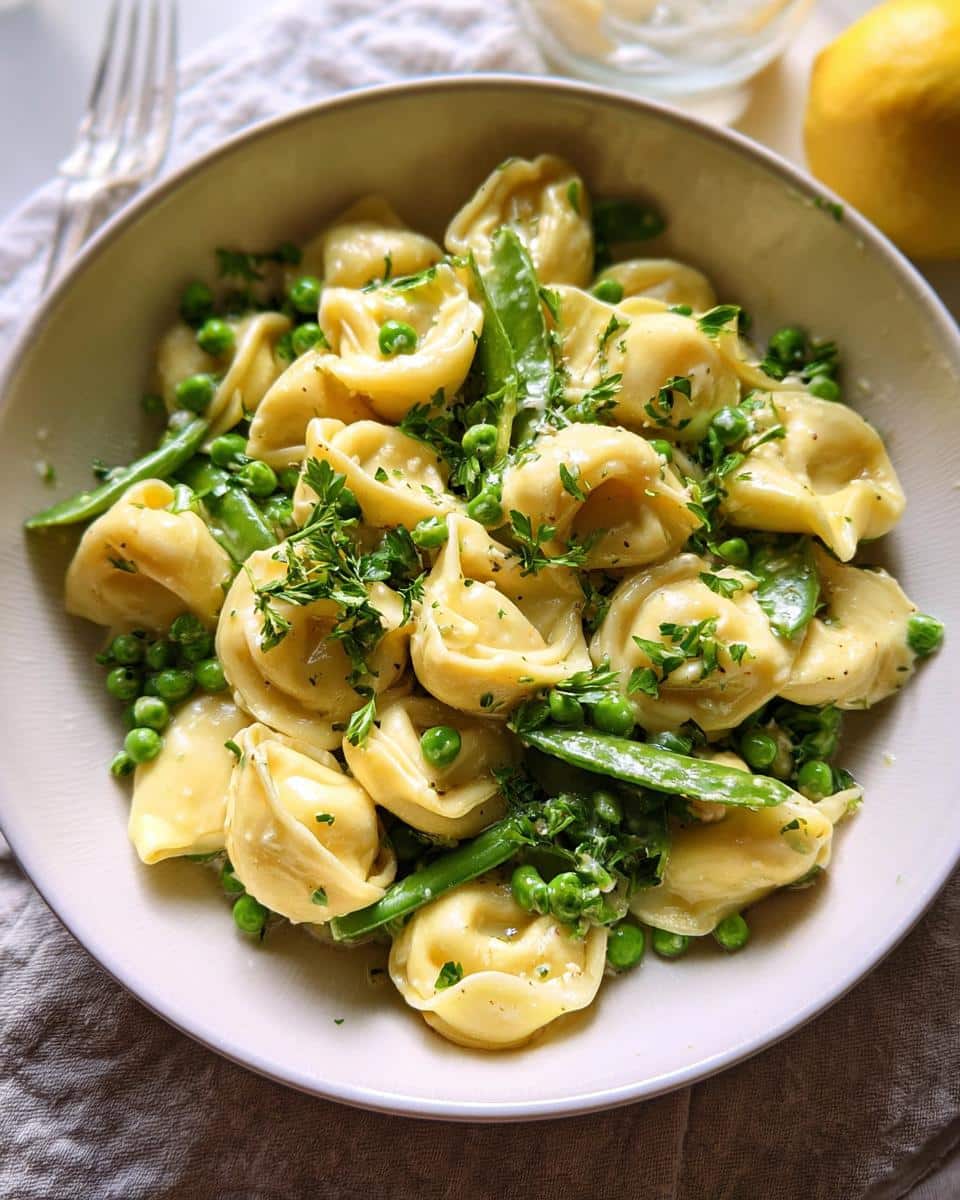 Close-up of a bowl filled with Lemon Garlic Tortellini with Peas, tossed in a light sauce and garnished with fresh parsley.