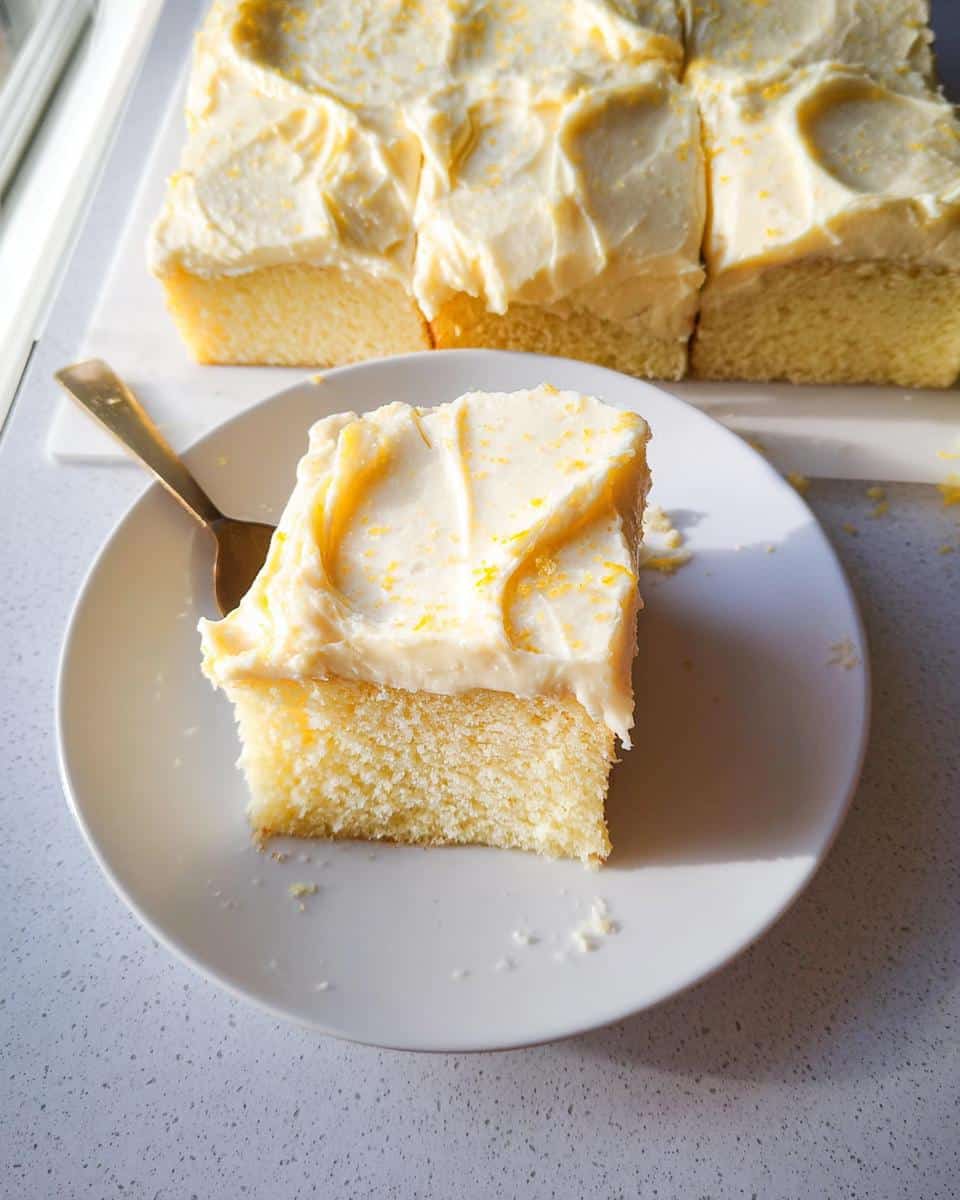 A square slice of moist Lemon Yogurt Sheet Cake topped with thick, creamy frosting and lemon zest.