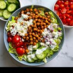 Top-down view of a vibrant Mediterranean Chickpea Lunch Bowl featuring seasoned chickpeas, feta, cucumbers, and dressing.