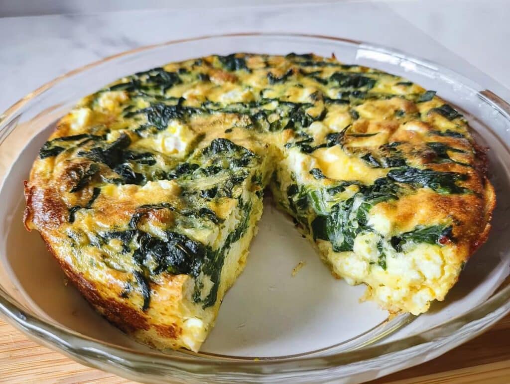 A baked Mini Crustless Spinach & Feta Tart in a glass dish, showing a wedge removed to expose the fluffy interior.