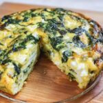 A baked Mini Crustless Spinach & Feta Tart, featuring visible spinach and white feta cheese chunks, resting on a wooden board.