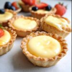 Close-up of several Mini Individual Custard Tarts with creamy yellow filling, some topped with fruit.