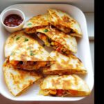 A plate filled with golden brown Mini Veggie Quesadillas, cut into triangles and showing a colorful vegetable filling.