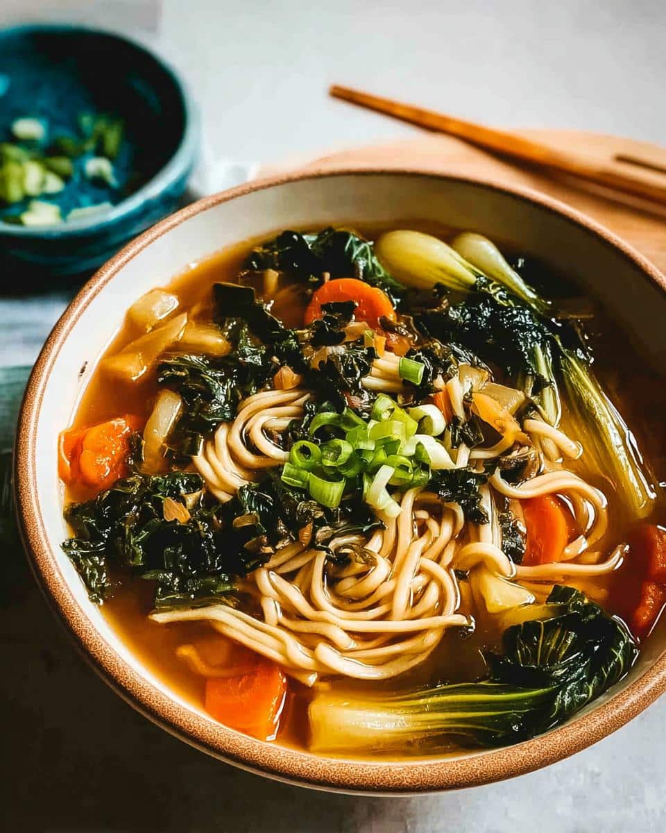 Close-up of a bowl of Miso Vegetable Soup featuring noodles, carrots, kale, and bok choy, topped with green onions.