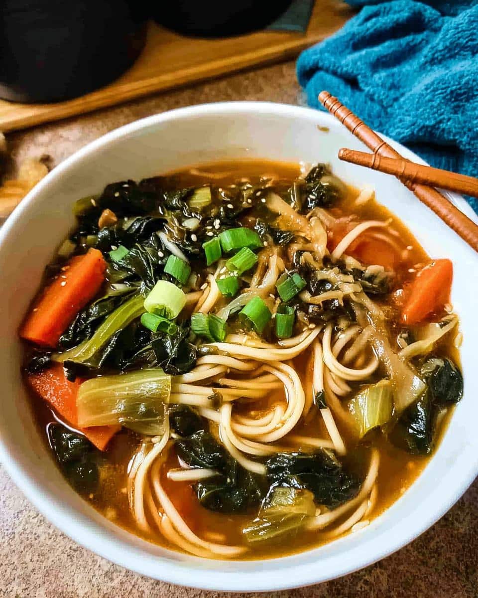Top-down view of a white bowl filled with Miso Vegetable Soup featuring noodles, dark leafy greens, carrots, and green onion garnish.