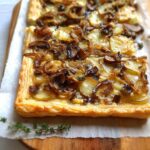 Close-up of a rectangular Mushroom Caramelized Onion Tart with sliced potatoes and fresh thyme garnish.