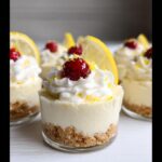 Close-up of individual No-Bake Lemon Cheesecake Cups topped with whipped cream, a cranberry, and lemon zest.